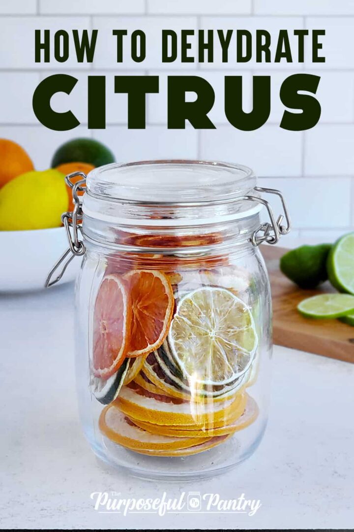 Glass jar full of dried citrus rounds on a wooden cutting board with cut lime, and whole lemon and orange