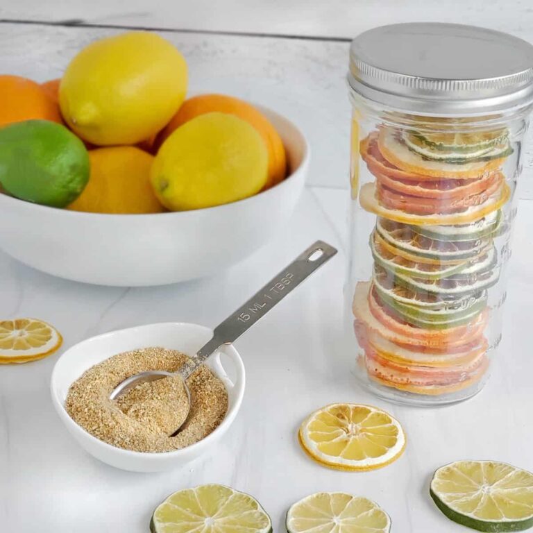 Canning jar of dried citrus slices, a dish of citrus powder and a bowl of citrus in the background.