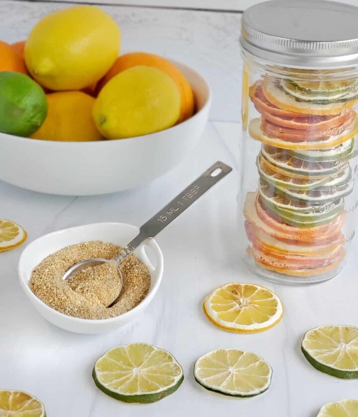 Canning jar of dried citrus slices, a dish of citrus powder and a bowl of citrus in the background.