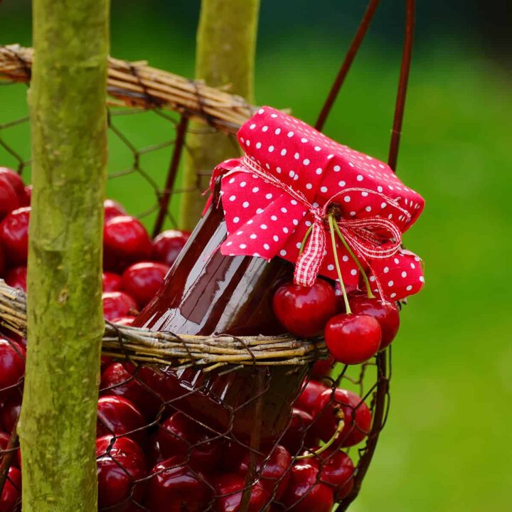 Cherries in a basket with a jar of cherry preserves with a red polka dot fabric cover