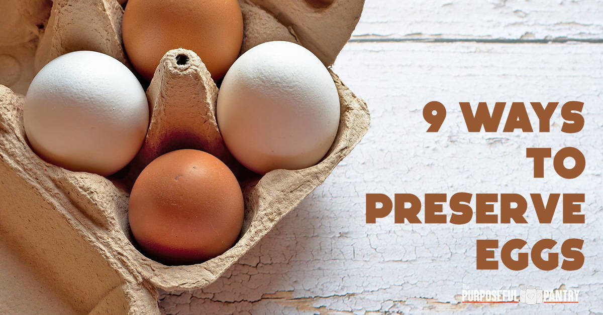 Brown and white naturally colored eggs in a paper carton on a white distressed table.