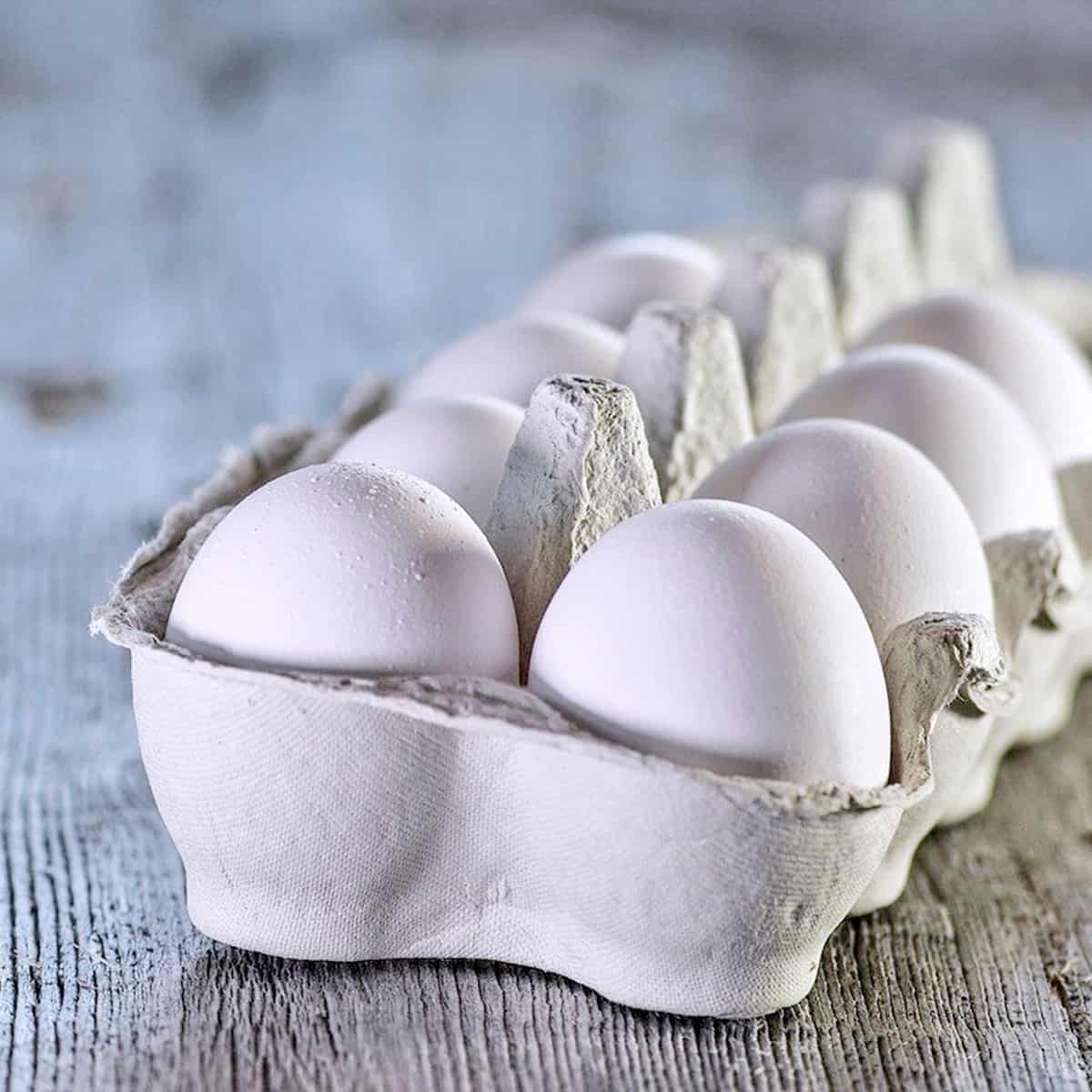 White eggs in a paper carton on a blue wooden surface