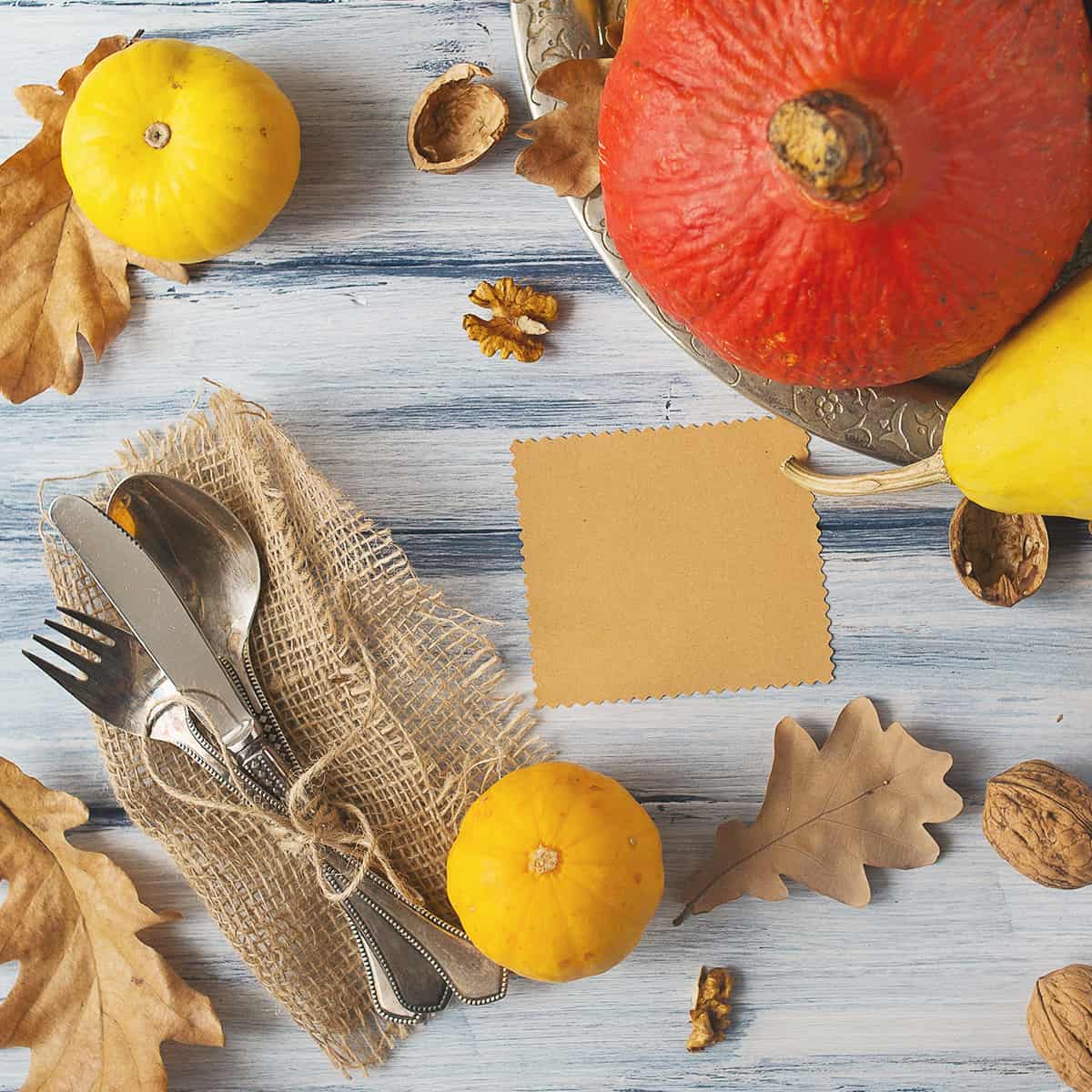 Thanksgiving tablescape from above - utensils, napkin, pumpkins a nd nuts on a wooden surface