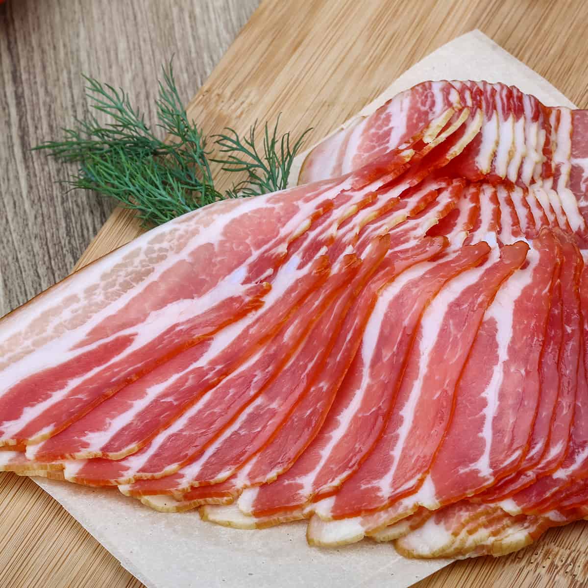 Bacon slices on a wooden surface with a sprig of an herb tucked inside.