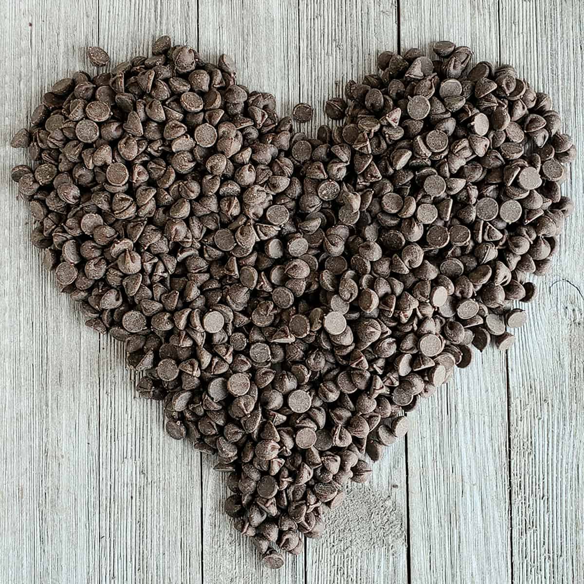 Chocolate chips in pile that have been formed into a heart-shape on a wooden surface