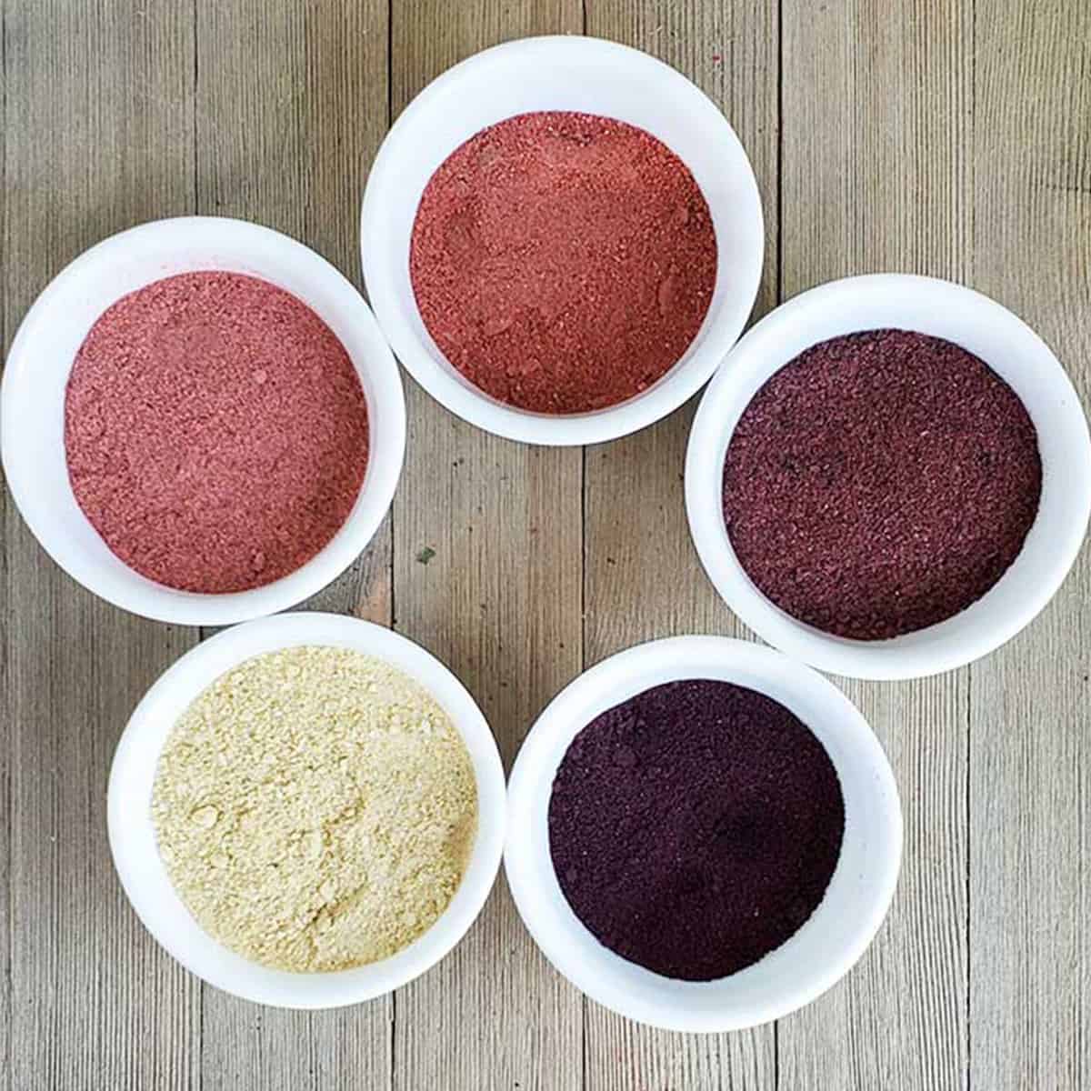 Strawberry, raspberry, blackberry, citrus, blueberry powders in white bowls on wooden background