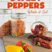 Mason jars of dehydrated sweet pepper dices, slices and whole on a wooden surface with fresh peppers in the foreground