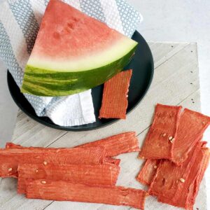 Watermelon slice on a blue plate with napkin and slices of dehydrated watermelon jerky