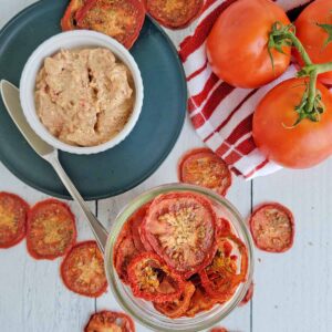 Herbed Garlic & Tomato sandwish spread on blue plate with dried tomato slices and fresh tomatoes