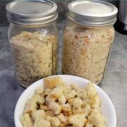 Homemade bread crumbs in mason jars and homemade croutons in a white bowl, all from the dehydrator