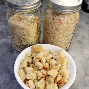 Homemade bread crumbs in mason jars and homemade croutons in a white bowl, all from the dehydrator
