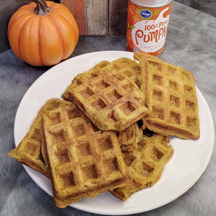 Stack of pumpkin waffles with canned pumpkin puree and some pumpkin decor in the background