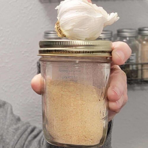 Canning jar of homemade garlic powder with garlic bulb