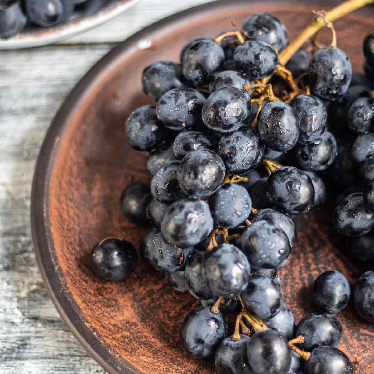 Plate of grapes on the stem on a wooden surface.