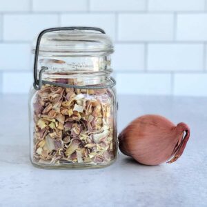 Dehydrated shallots in an old canning jar with a large shallot on the table top