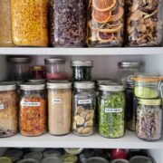 Jars of dehydrated foods on a white bookshelf.