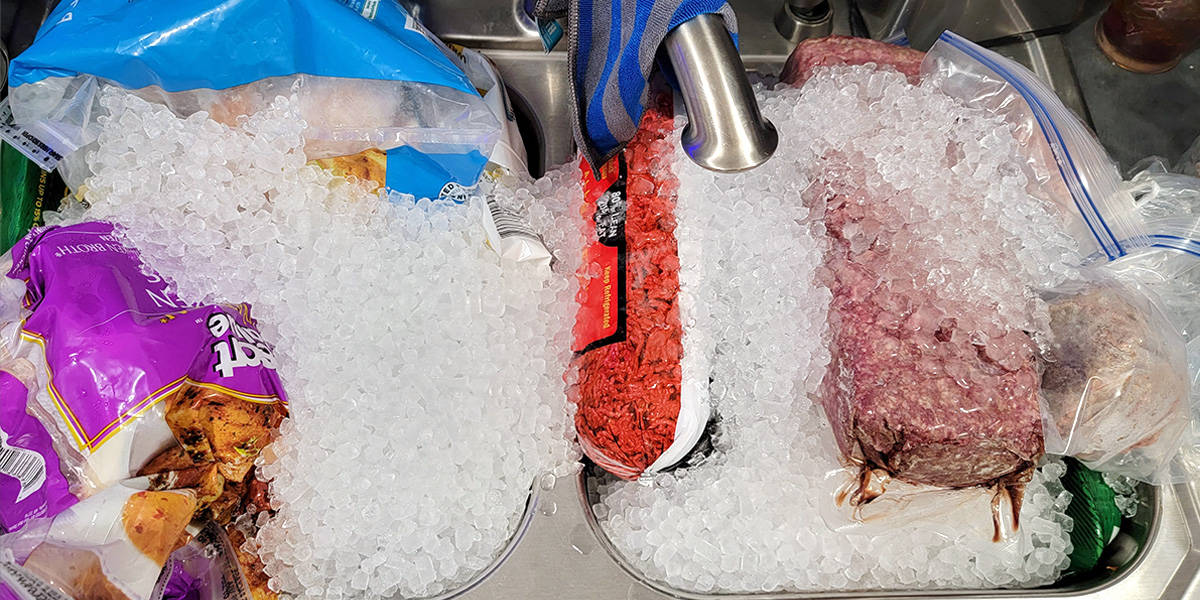 Refrigerated meats from small fridge and freezer in a kitchen sink with ice to protect it during power outage.