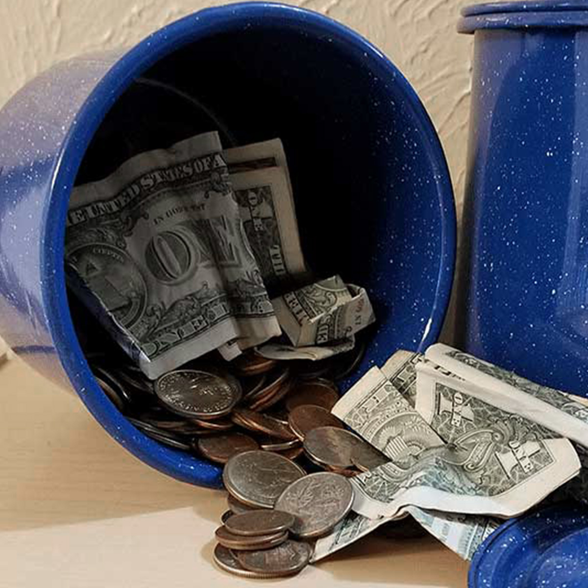 Dollar bills and change inside a storage container for saving an emergency fund.