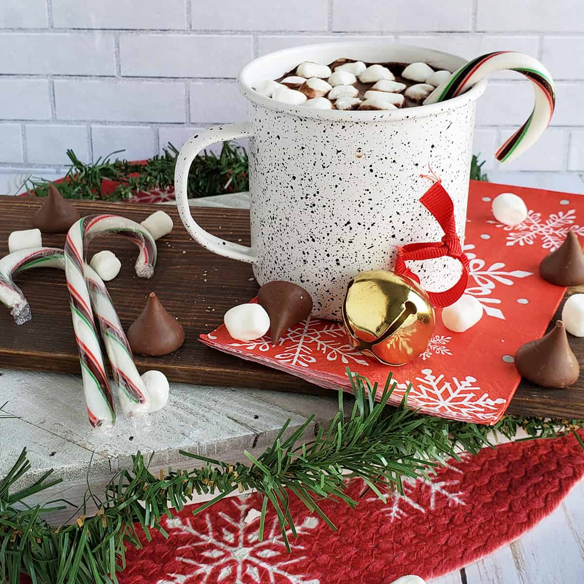 Hot cocoa mix on with marshmallows and a peppermint stick on a Christmas tablescape.