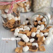 Crunchy s'more mix in a gift jar and spilling out on a white table.