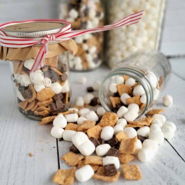 Crunchy s'more mix in a gift jar with a red ribbon and spilling on a white table top.