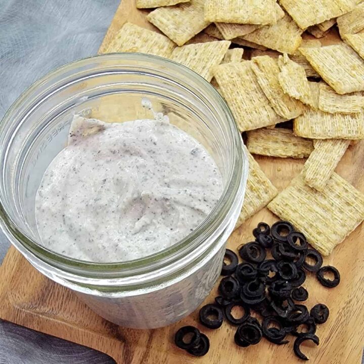 Olive powder dip in a mason jar on a plate with crackers and dehydrated olives