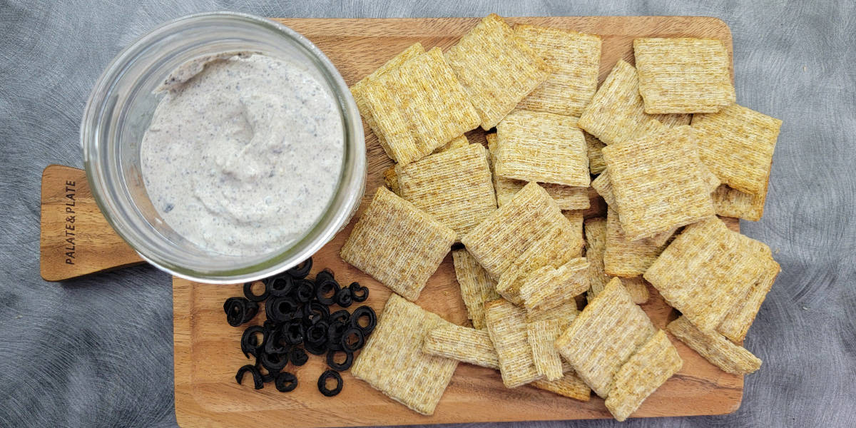 Olive powder dip on a serving tray with Triscut crackers and dehydrated olive slices