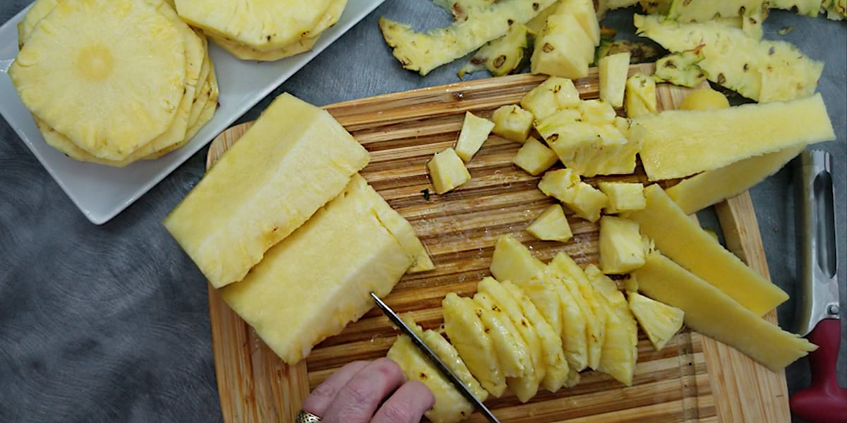 Pineapple being cut on a wooden cutting board.