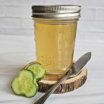 Cucumber jelly on a wooden disc with fresh cucumber slices on a white background with a stainless steel knife.