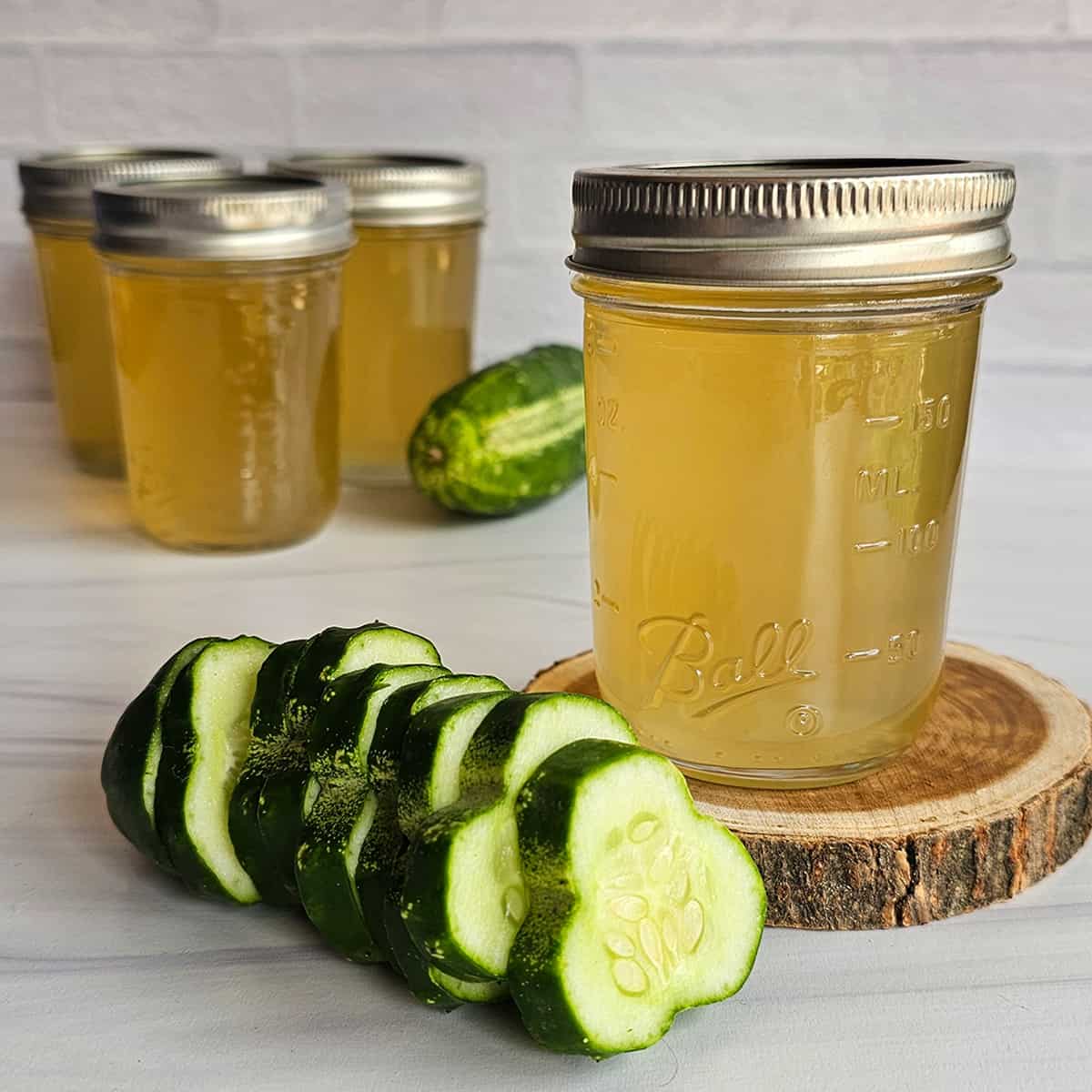 Cucumber jelly on a wooden disc with fresh cucumbers, and jars of jelly in the background.