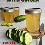 Cucumber jelly on a wooden disc with fresh cucumbers, and jars of jelly in the background.