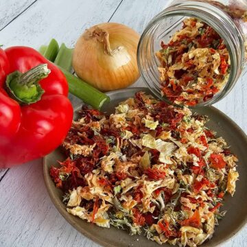 A jar of mixed vegetables on a table next to a red pepper.