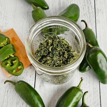 A jar of dried, green jalapeno peppers on a wooden table.