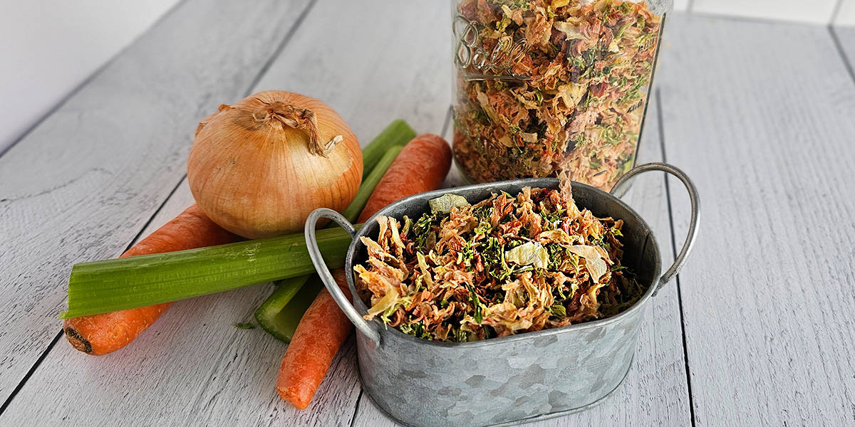 A container of dried mirepoix with carrots, celery and onions on a wooden table.