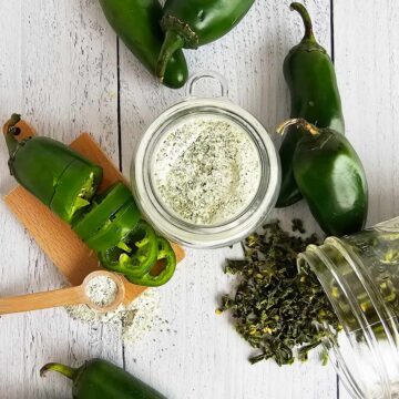 Jalapeno salt surrounded by fresh and dried jalapenos on a white table.