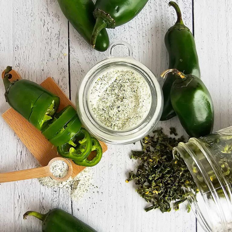 Jalapeno salt surrounded by fresh and dried jalapenos on a white table.