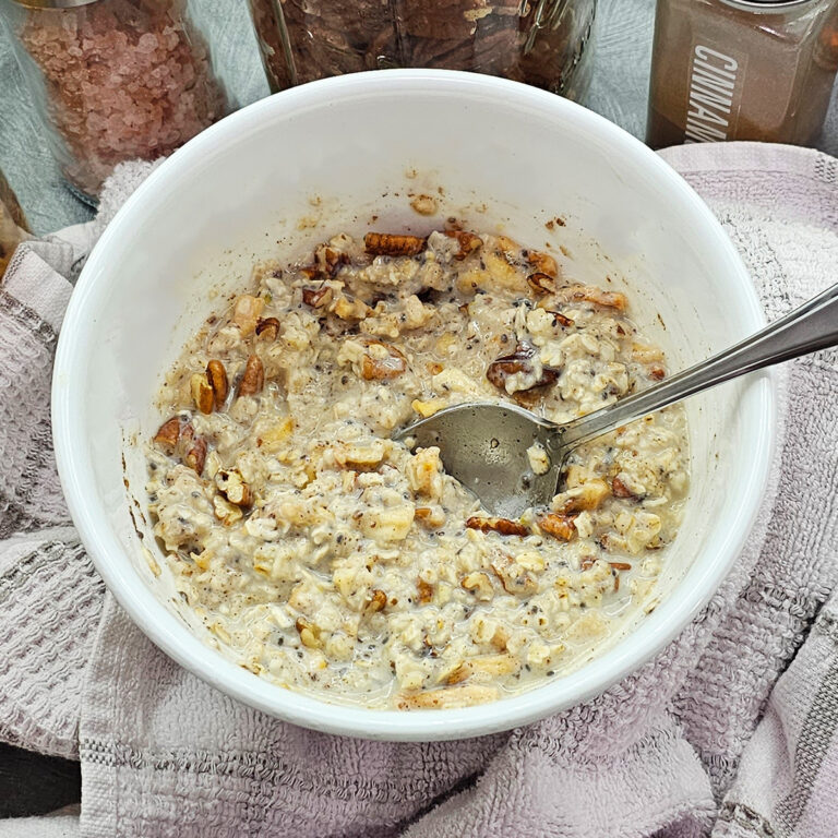 Oatmeal in a white bowl with nuts, dehydrated apples, and a spoon.