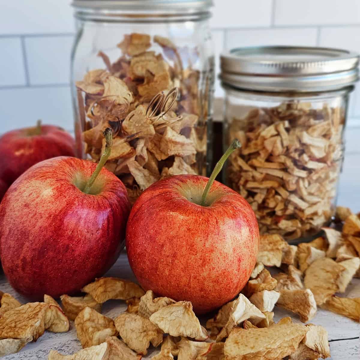 Apple chips in jars and apples on a table.