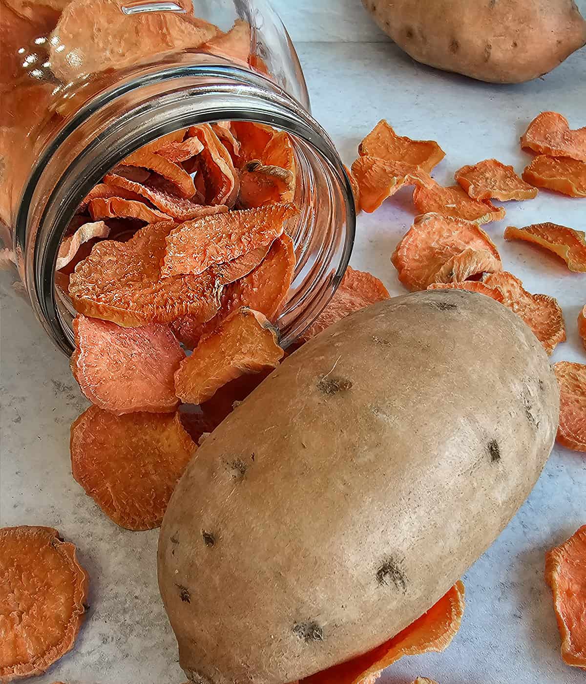 Sweet potato chips in a jar with fresh sweet potato.