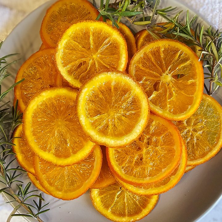 Sliced oranges on a plate with rosemary sprigs.