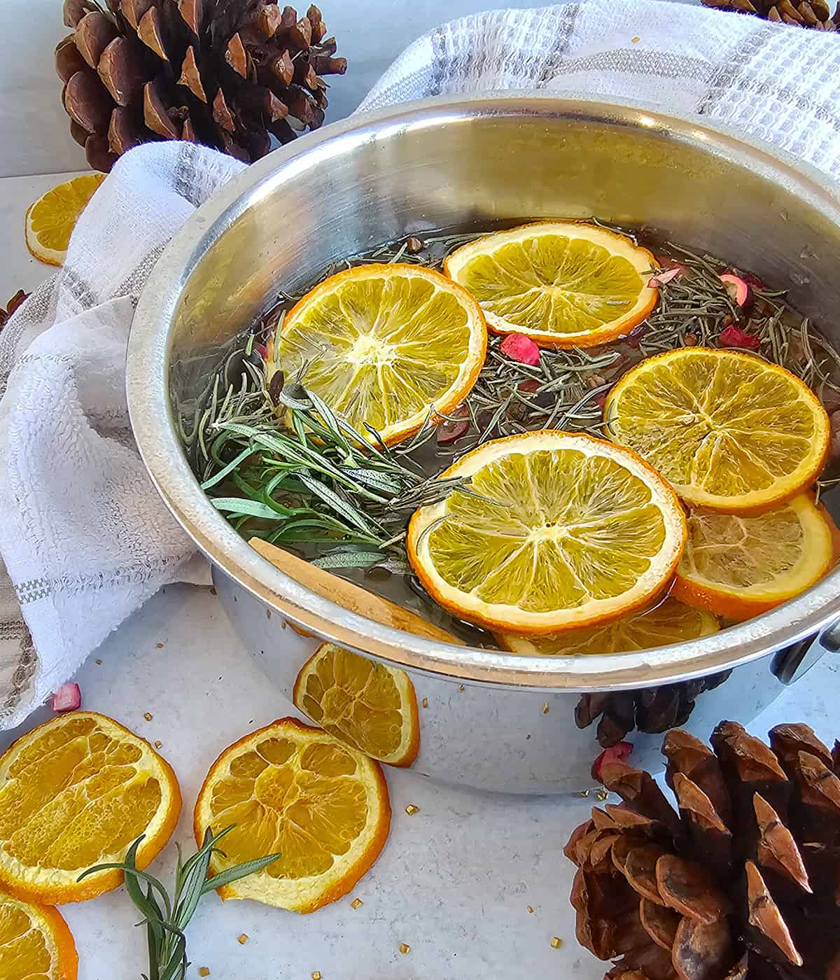 A bowl filled with dried orange slices and herbs with pinecones on the table.
