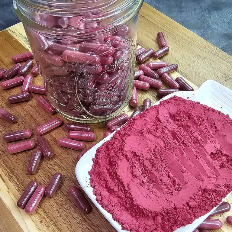 A jar of beet capsules next to a white plate of beet powder.