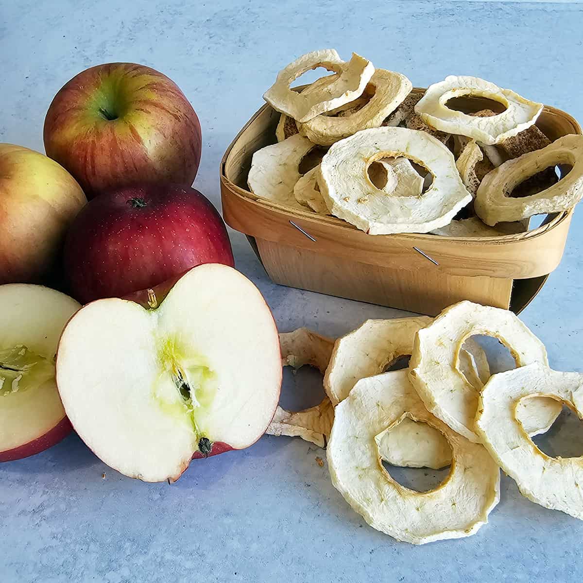 Dried apple rings in a basket with fresh apples on the table.