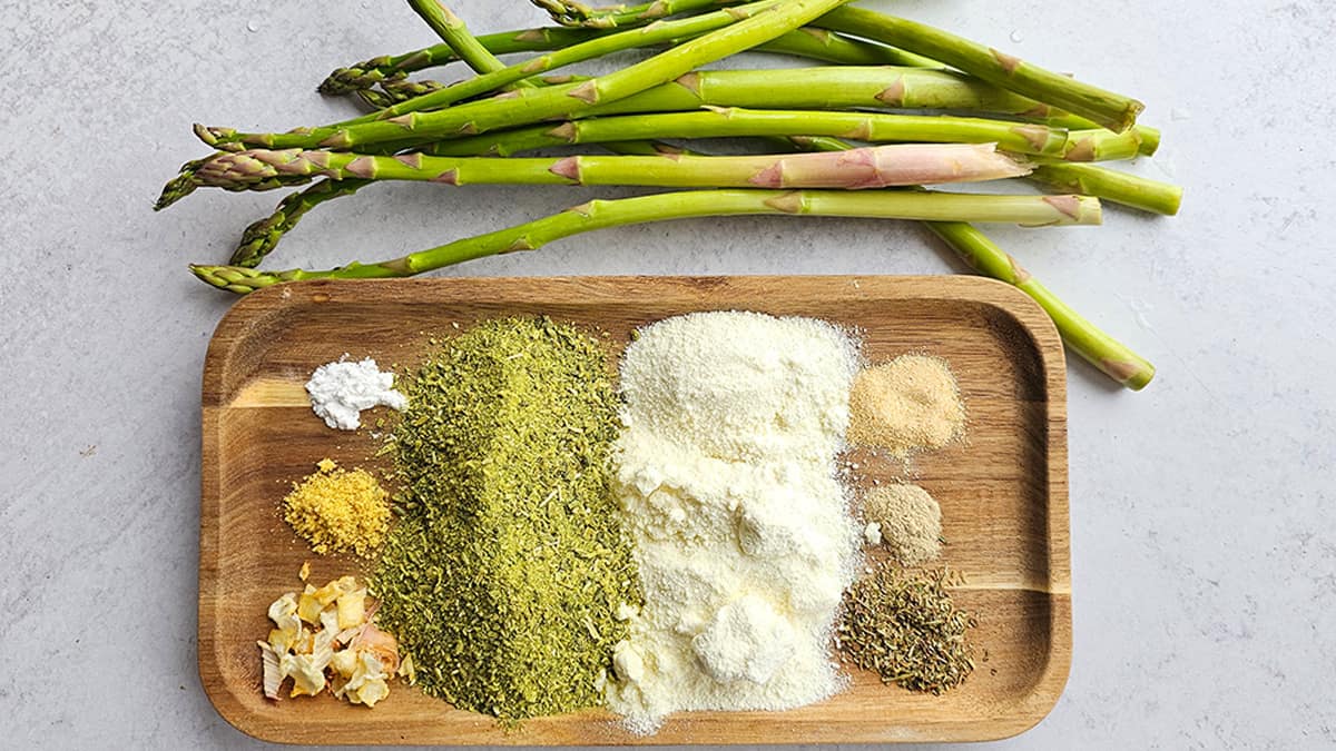 Various spices and fresh asparagus on a wooden cutting board.