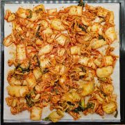 Chopped kimchi spread evenly on a dehydrator tray, displaying red seasoning and pieces of napa cabbage.