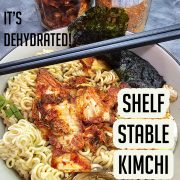A bowl of ramen topped with dehydrated kimchi and vegetables, garnished with seaweed, with jars of dehydrated kimchi and kimchi powder in the background.